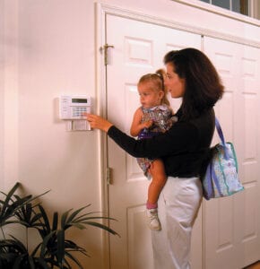 Woman holding child, entering code on home security keypad.